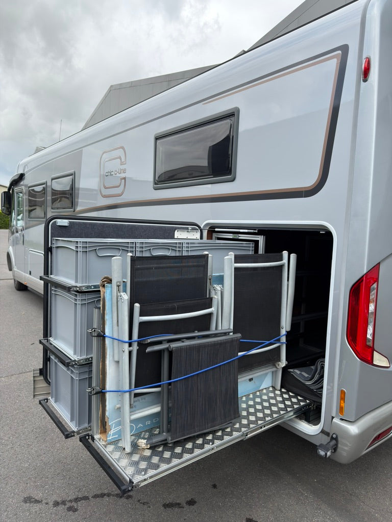 Uitgeschoven opbergsysteem met grijze bakken en kampeerstoelen in de zijgarage van een mobilhome